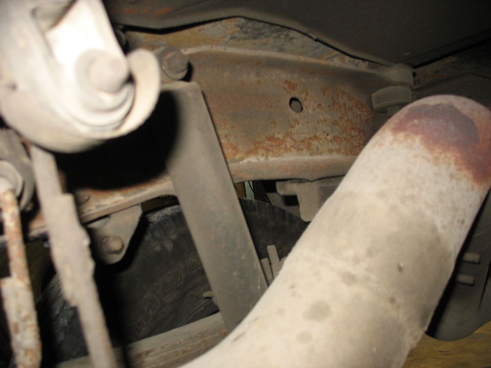 Close-up of vehicle undercarriage with rusted metal and exhaust pipe.