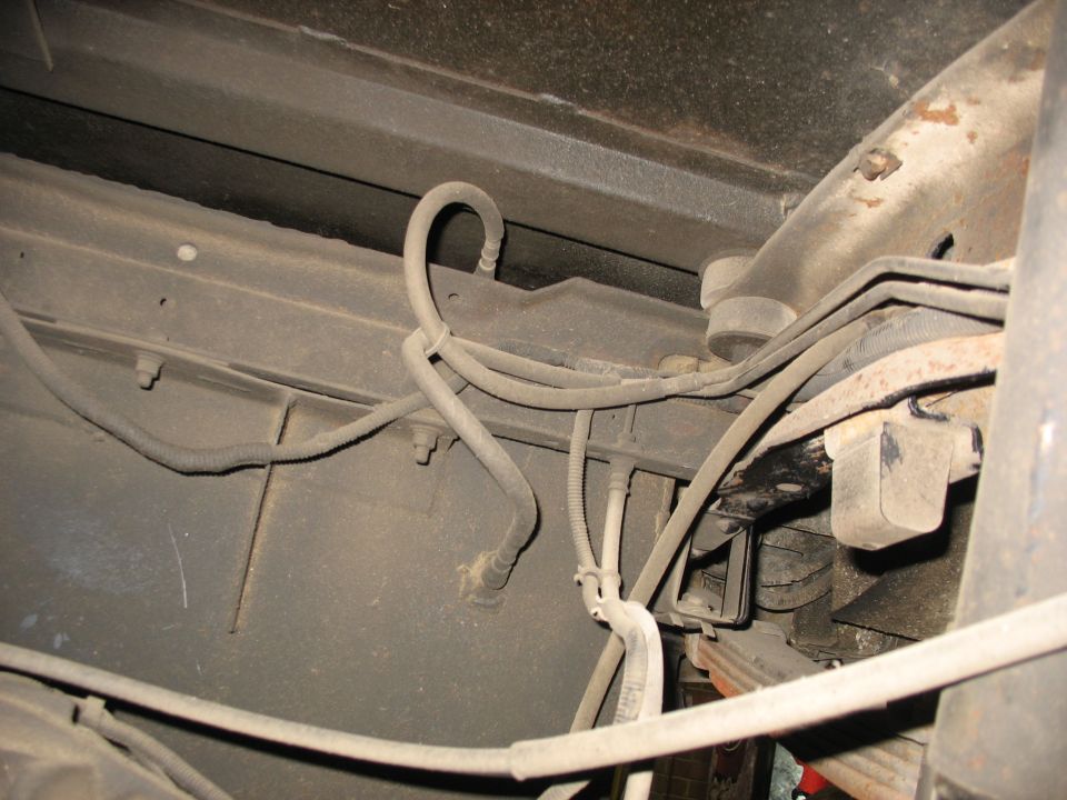 Underside of a vehicle showing frame, suspension, brake lines, and wiring.