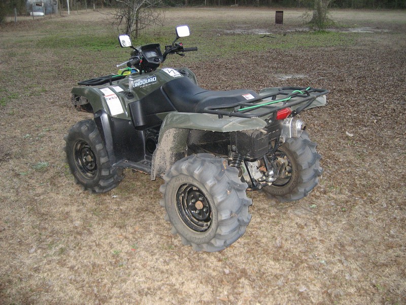 Green Suzuki KingQuad ATV with mud tires and rear snorkel parked on dry grass