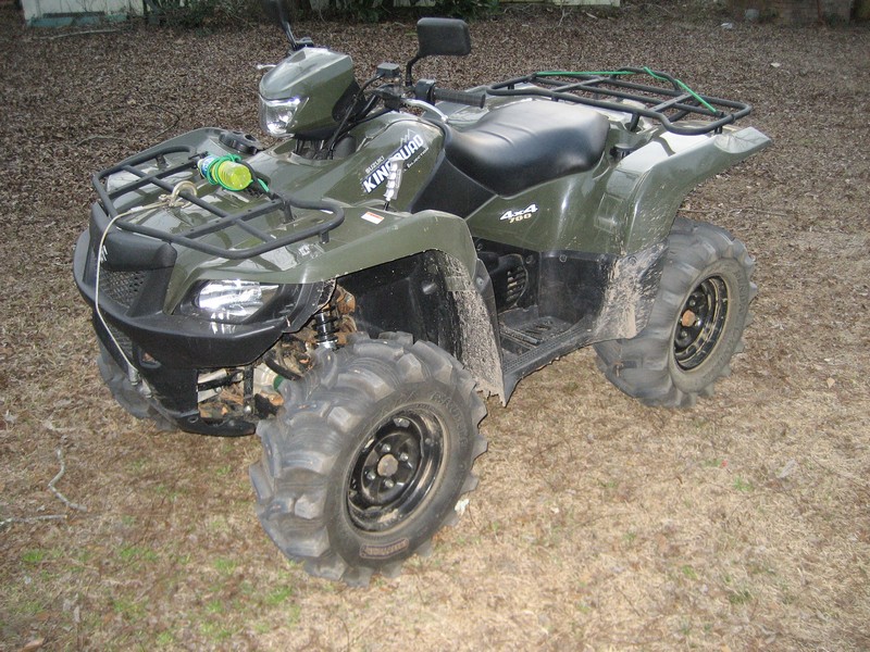 Green Suzuki KingQuad 4x4 700 ATV on pine straw with mud tires and camo shock covers
