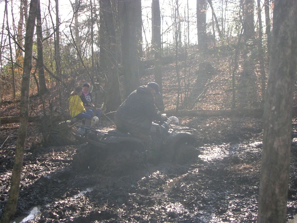 Rider on a mud-covered ATV powering through a mud pit in winter woods