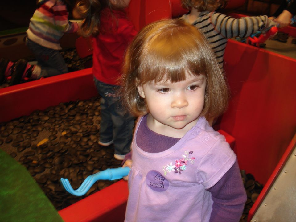 Young girl with blonde hair and bangs wearing a purple shirt, holding a blue toy.
