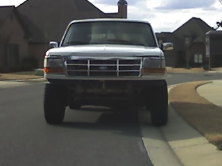 1996 Ford Bronco - Front view of a lifted white Ford Bronco parked on a residential street. The vehicle has large tires and appears to be a 1990s model.