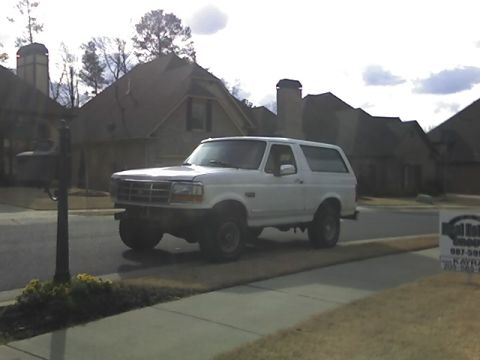 1996 Ford Bronco - A white, two-door Ford Bronco is parked on a residential street in front of several houses. The vehicle is viewed from a three-quarter fron…