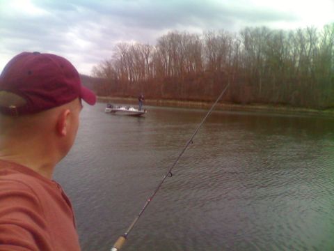 1996 Ford Bronco - A person wearing a red baseball cap and orange shirt is fishing on a body of water. Another person is visible on a boat in the distance.