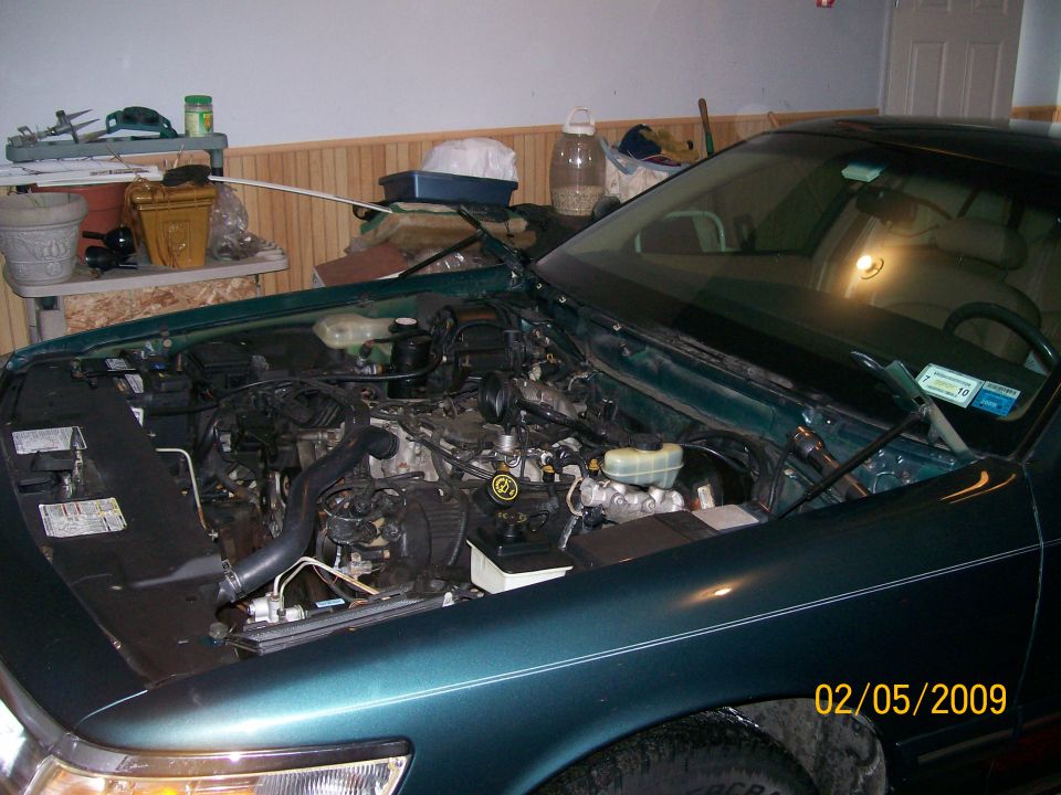 Green car engine bay with hood open inside a garage