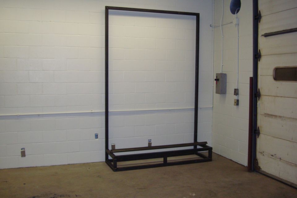Welded rectangular steel frame standing in a shop near an overhead door