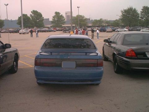 2000 Ford Crown Victoria - A blue sedan with a spoiler is parked in a lot next to a dark police car.