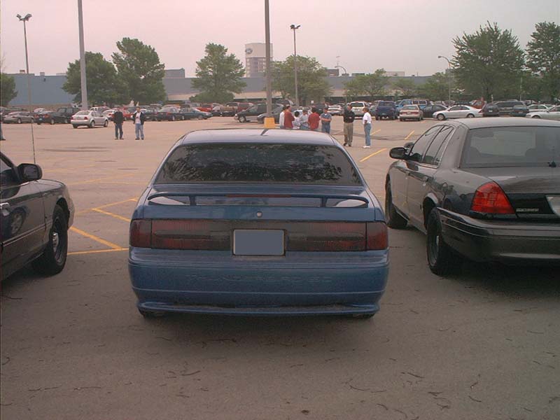 Blue sedan parked in a lot, rear view. It has a spoiler and tinted taillights