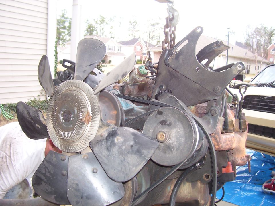 V8 engine with fan shroud and pulley system, suspended by chains.