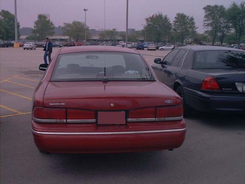 2000 Ford Crown Victoria - Straight-on rear view of a red first-generation (aero-body) Ford Crown Victoria sedan with full-width chrome-trimmed taillamps and a blanke…