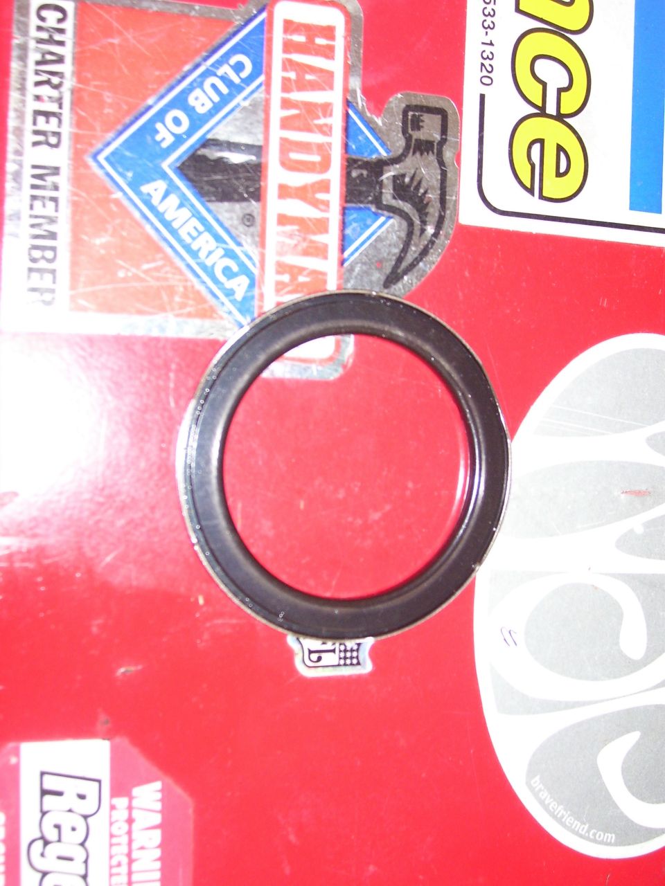 Black circular gasket on a red surface with stickers.