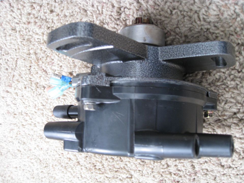 Black automotive distributor cap with gray bracket assembly on carpet