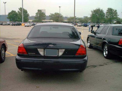 2000 Ford Crown Victoria - Two black Ford Crown Victorias are parked side-by-side in a large outdoor parking lot.