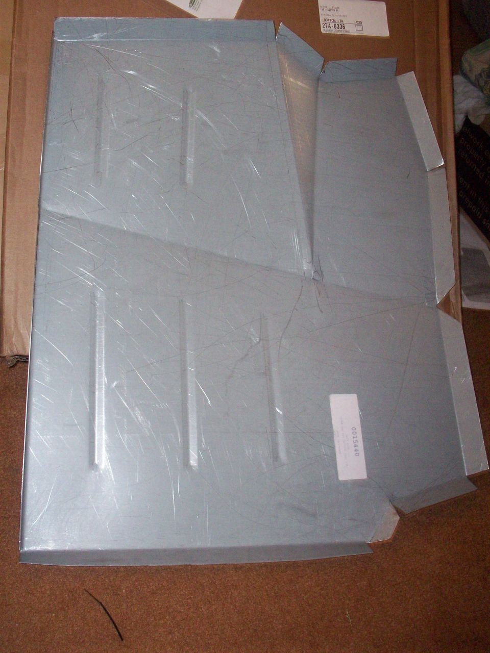 Gray metal floor pan part with reinforcing ribs and a label.
