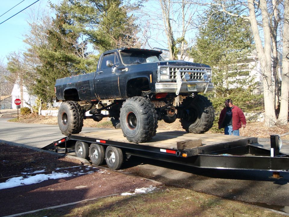 Lifted black pickup truck on a trailer with a man standing nearby.
