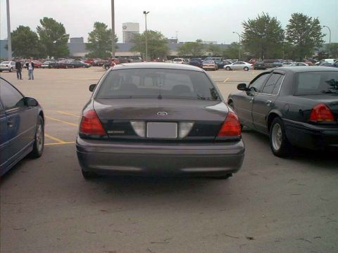 2000 Ford Crown Victoria - Two Ford Crown Victorias and a blue sedan are parked in a lot under an overcast sky.
