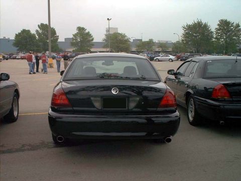 2000 Ford Crown Victoria - A black sedan is parked in a lot, showing its rear end with dual exhaust pipes and a Mercury emblem.