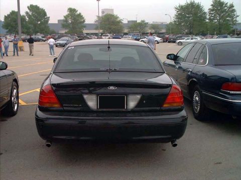 2000 Ford Crown Victoria - The rear of a black 2000 Ford Crown Victoria LX is visible in a parking lot, parked next to another vehicle.