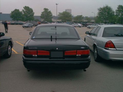 2000 Ford Crown Victoria - Two Ford Crown Victorias are parked side-by-side in a parking lot under an overcast sky.