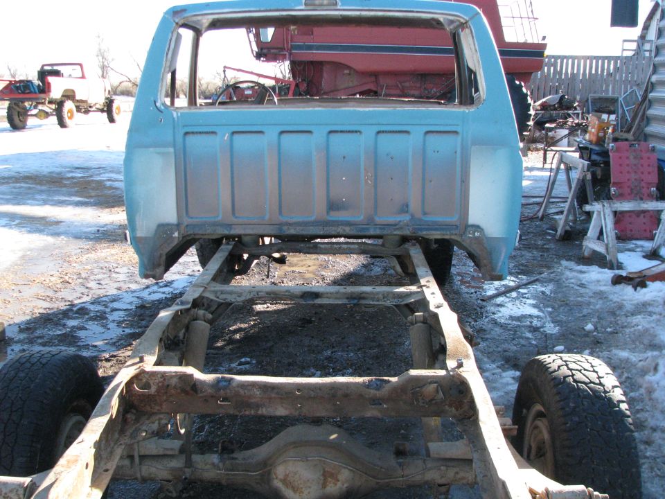 Rear view of a light blue pickup truck cab and chassis with no bed, outdoors in a snowy, muddy area.