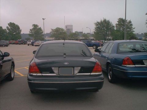 2000 Ford Crown Victoria - Two Ford Crown Victorias parked in a lot, one dark green and one blue.