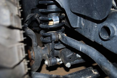 2008 Jeep Wrangler - A close-up view of the front suspension of a 2008 Jeep Wrangler, showing the coil spring, sway bar end link, and part of the tire.
