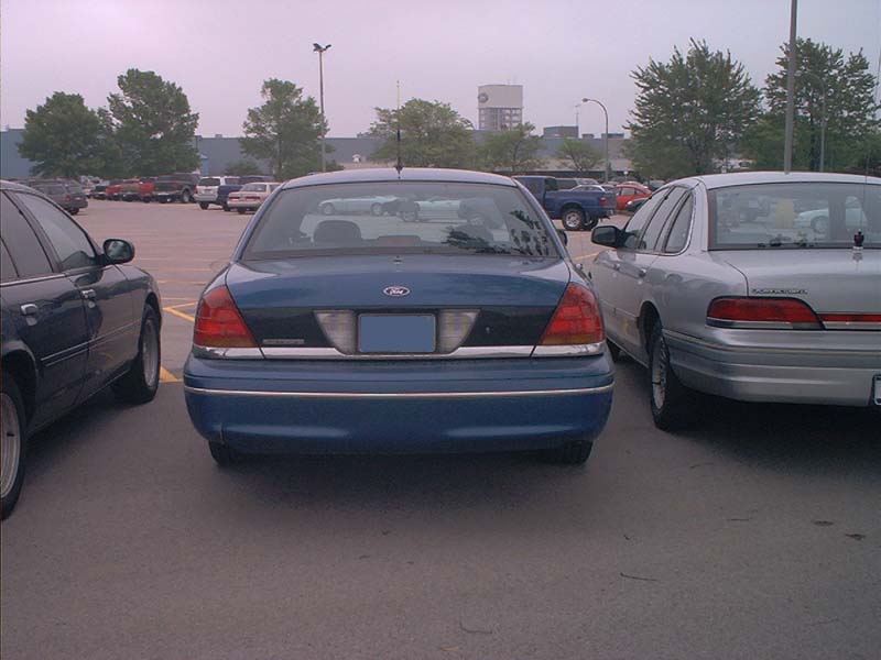 Blue Ford Crown Victoria parked in a lot next to a silver one. Rear view