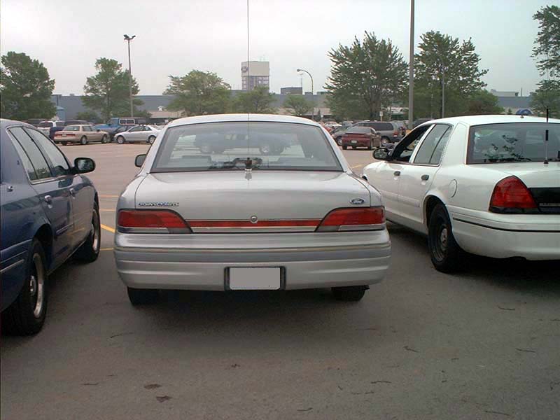 Silver 2000 Ford Crown Victoria parked between a blue sedan and a white police car