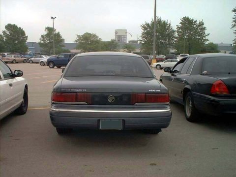 2000 Ford Crown Victoria - A Mercury Grand Marquis is parked in a lot. The car is dark gray with chrome accents.