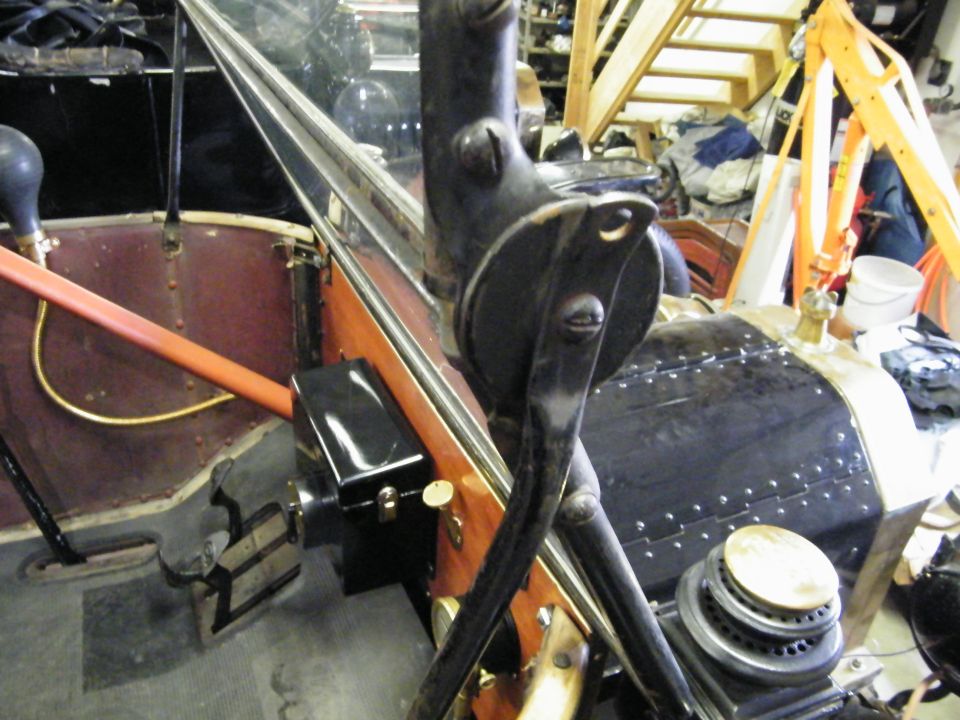 Interior of a vintage car showing steering column, dashboard, and engine hood.