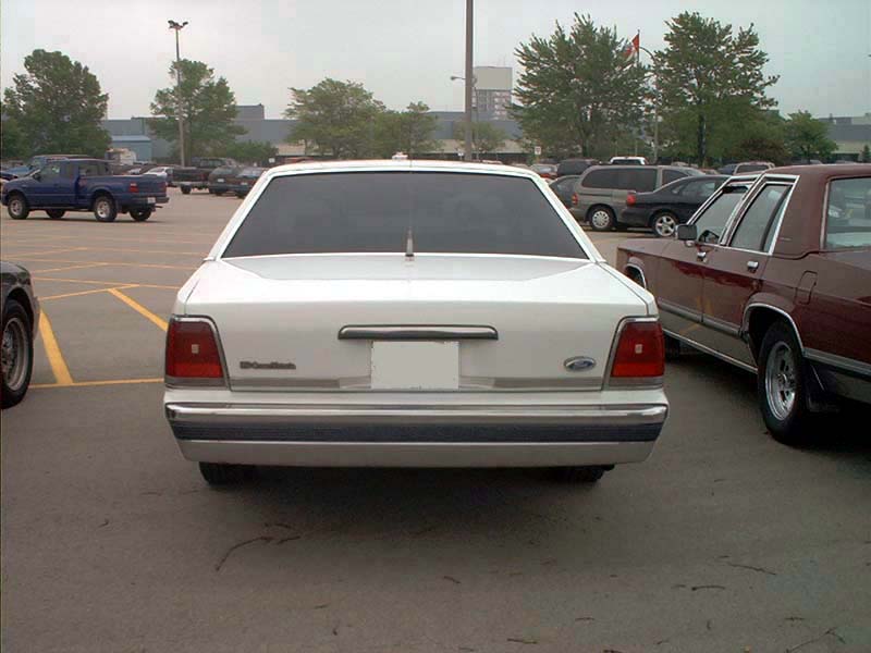 White 2000 Ford Crown Victoria, rear view, parked in lot. Chrome bumper, tinted windows