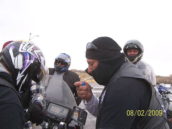 Motorcycle riders in helmets and balaclava standing by their bikes on a gray day