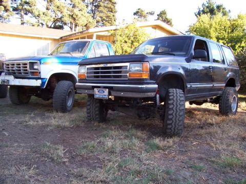 1977 Ford F-150 - A lifted dark blue Ford Explorer is parked next to a lifted blue and white Ford F-150 pickup truck. Both vehicles are parked on a dirt and…