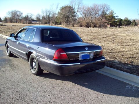 1999 Mercury Grand Marquis - The rear driver's side quarter of a dark blue Mercury Grand Marquis sedan is shown parked on an asphalt road next to a grassy field.