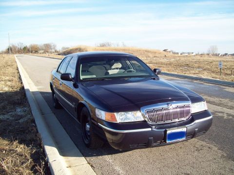 1999 Mercury Grand Marquis - A dark blue Mercury Grand Marquis sedan is parked on the side of a paved road next to a concrete curb. The vehicle is facing forward, with…