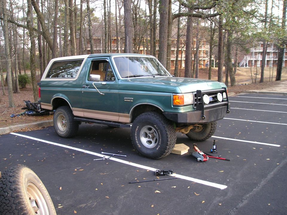 Green Ford Bronco on jack with front wheel removed and tools on pavement