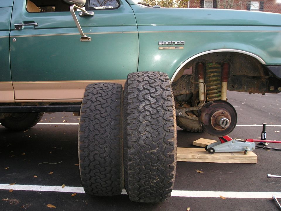 Green Ford Bronco jacked up with front wheel off, exposing coil spring and hub