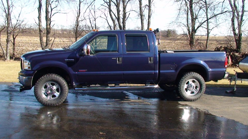 Dark blue Ford F-350 crew cab pickup truck with chrome wheels towing a trailer.