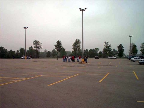 2000 Ford Crown Victoria - A group of people gather in a large, mostly empty parking lot on an overcast day.