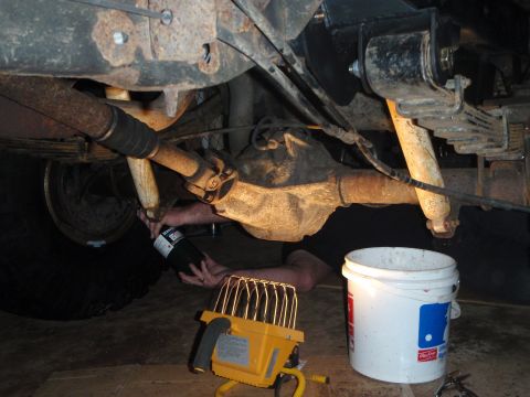 1996 Ford Bronco - A person is working underneath a vehicle, holding a can of fluid over a white bucket. The vehicle appears to be a truck or SUV with a leaf…