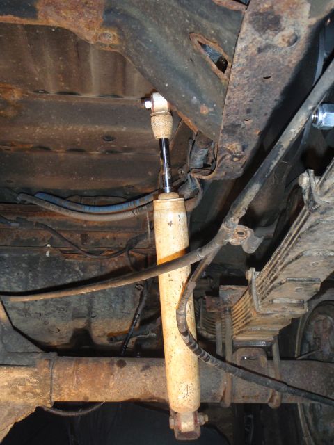 1996 Ford Bronco - The underside of a vehicle shows a rusty leaf spring and a shock absorber attached to the frame and axle. Various hoses and wires are also…
