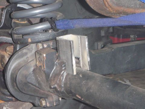 1996 Ford Bronco - A close-up view of a custom metal bracket welded onto the axle of a 1996 Ford Bronco, with a blue strap wrapped around the suspension sprin…