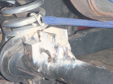 1996 Ford Bronco - A close-up view shows a welded bracket attached to a vehicle's suspension component, with a blue strap wrapped around a coil spring.