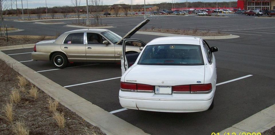 Photo of a white Crown Victoria with door open and a tan Grand Marquis in a parking lot