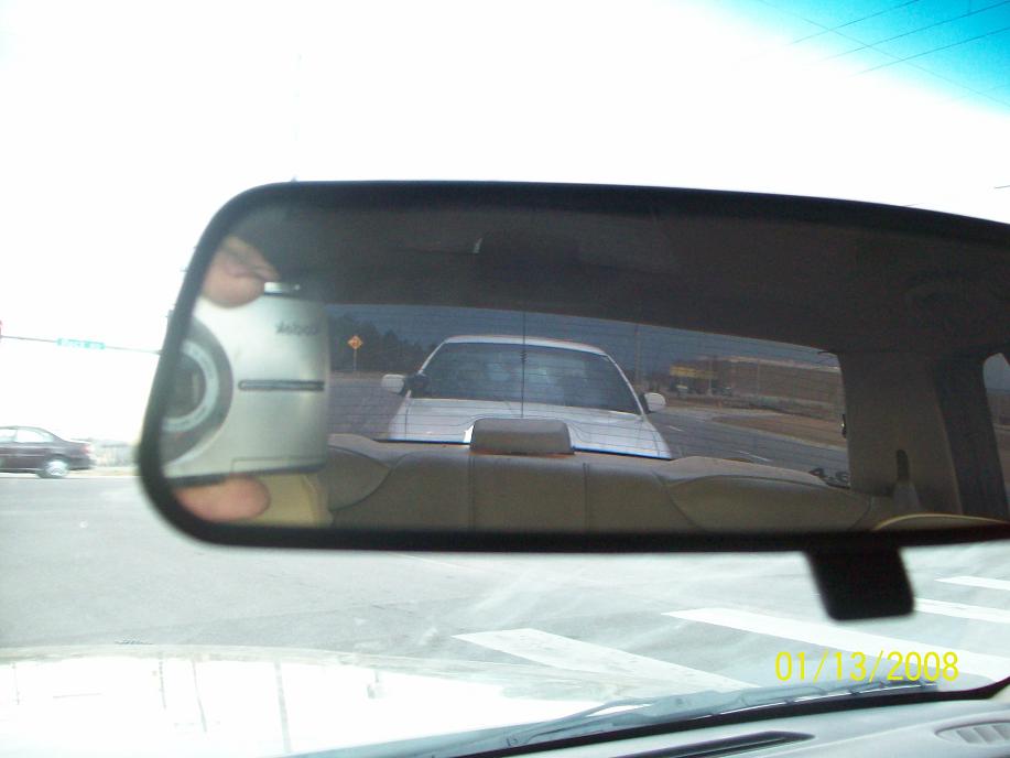 Rearview mirror reflecting a car following behind on a road