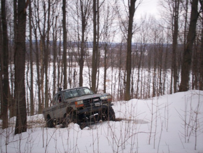 Lifted gray pickup with front winch crawling through snow in bare woods