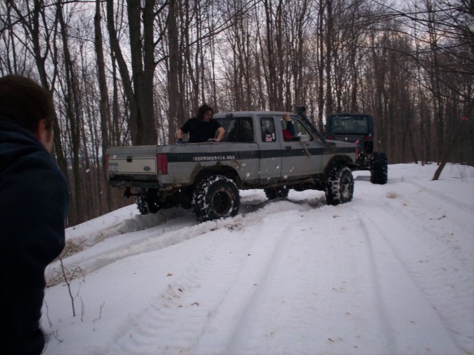 Lifted silver and green Ford pickup on mud tires climbing a snowy wooded trail