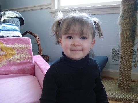 2000 Ford Crown Victoria - A young child with blonde hair in pigtails smiles at the camera while wearing a black turtleneck. The child is sitting in a pink chair with…