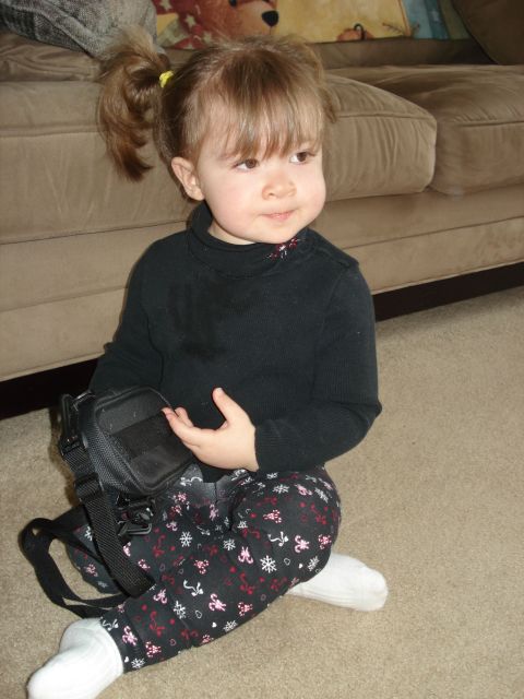 2000 Ford Crown Victoria - A young girl with blonde hair in pigtails sits on a carpeted floor holding a small black bag. She is wearing a black turtleneck and pattern…